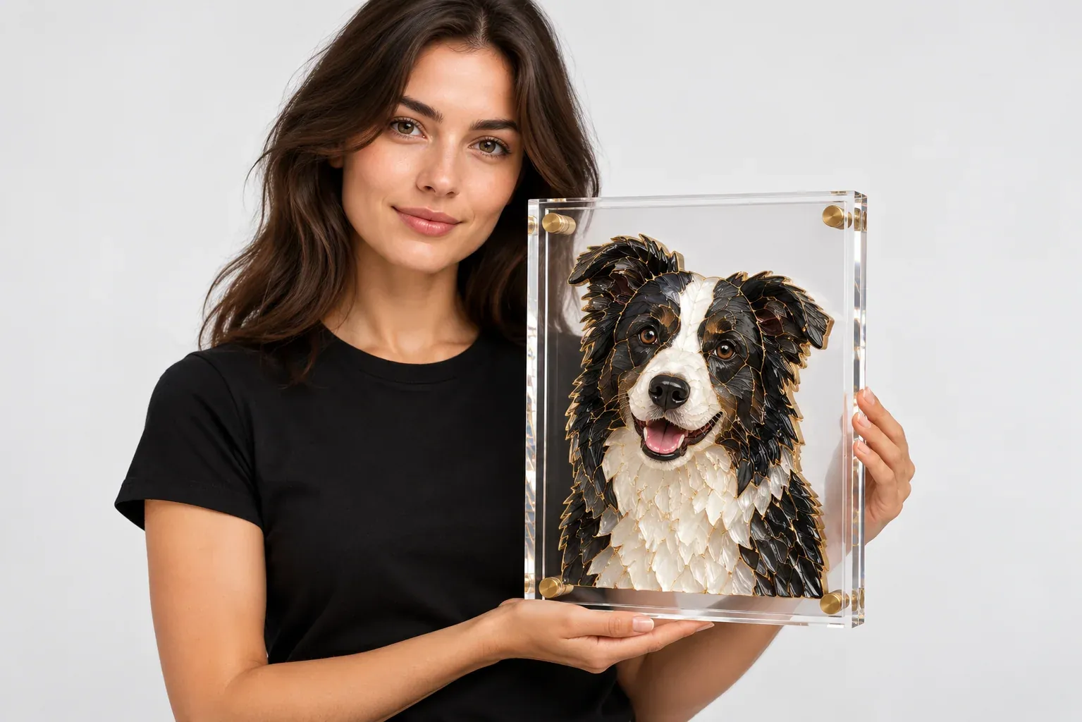 A woman in a black T-shirt holding her border collie's mosaic portrait in a clear acrylic block, on a light grey backdrop